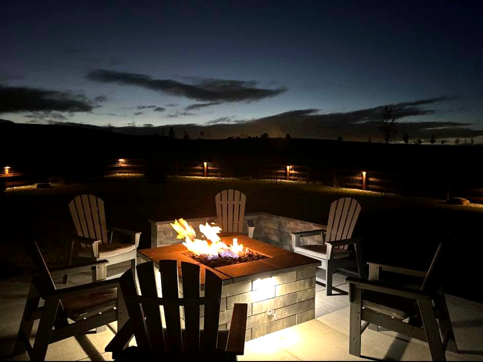Lit fire pit and fence lighting glowing at dusk